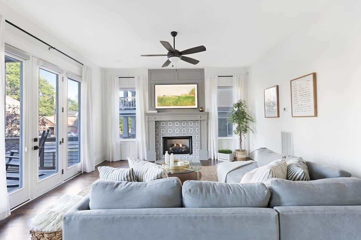 A modern living room with a fireplace, a ceiling fan, and a large window overlooking a deck.