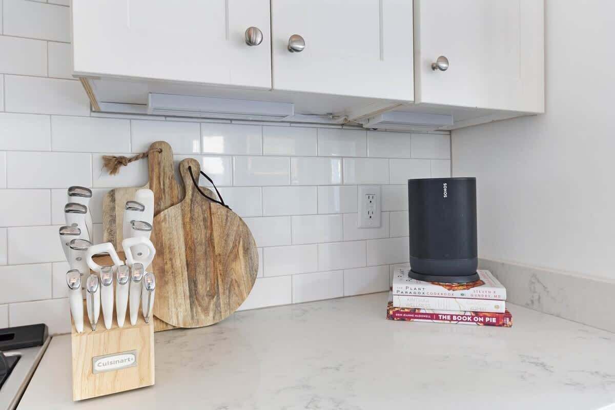 A kitchen with white cabinets, a wooden cutting board, a knife set, and a stack of cookbooks.