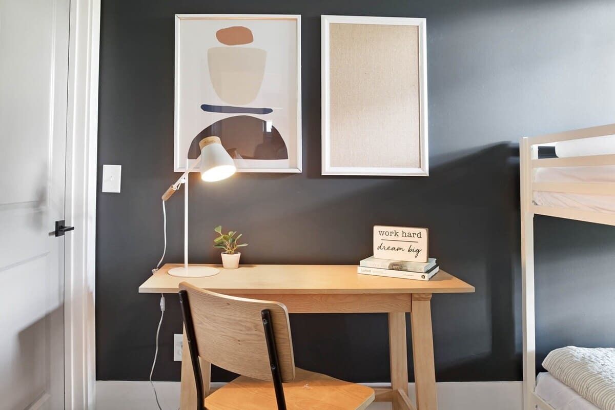 A bedroom with a bunk bed, a desk with a chair, a lamp, a small plant, and two framed pictures on the wall.