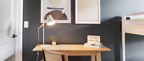 A bedroom with a bunk bed, a desk with a chair, a lamp, a small plant, and two framed pictures on the wall.