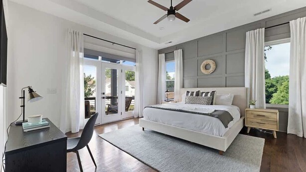 A bedroom with a bed, a desk, a chair, a ceiling fan, and a view of the outdoors.