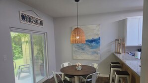 A dining area with a round table, white chairs, a hanging light fixture, and a painting on the wall. - SALE Aug & Sept dates 15% off!! Come enjoy Gulf Shores in comfort with us. (Gulf Shores)