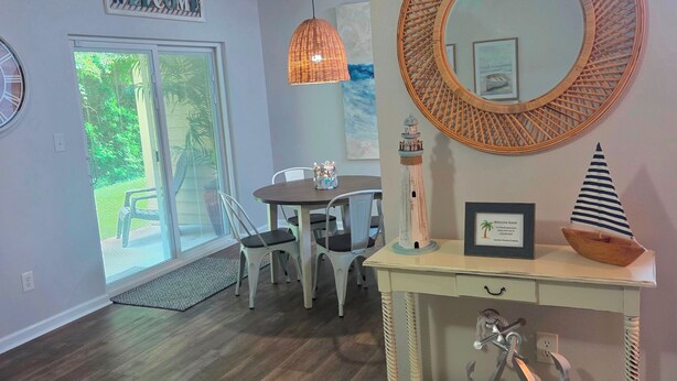 A room with a dining table, chairs, a console table with a mirror, and a large window with blinds. - SALE Aug & Sept dates 15% off!! Come enjoy Gulf Shores in comfort with us. (Gulf Shores)