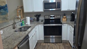 A modern kitchen with white cabinets, stainless steel appliances, a granite countertop, and a wooden floor. - SALE Aug & Sept dates 15% off!! Come enjoy Gulf Shores in comfort with us. (Gulf Shores)