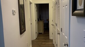 A hallway with white walls, wooden flooring, and a ceiling light. There are doors on both sides, and a framed picture on the left wall. - SALE Aug & Sept dates 15% off!! Come enjoy Gulf Shores in comfort with us. (Gulf Shores)