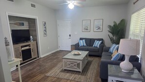 A living room with a TV, sofa, coffee table, and decorative items. - SALE Aug & Sept dates 15% off!! Come enjoy Gulf Shores in comfort with us. (Gulf Shores)