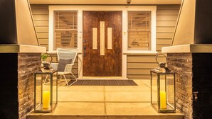 Una entrada principal amb una porta de fusta, una cadira blanca i dos fanals amb espelmes.