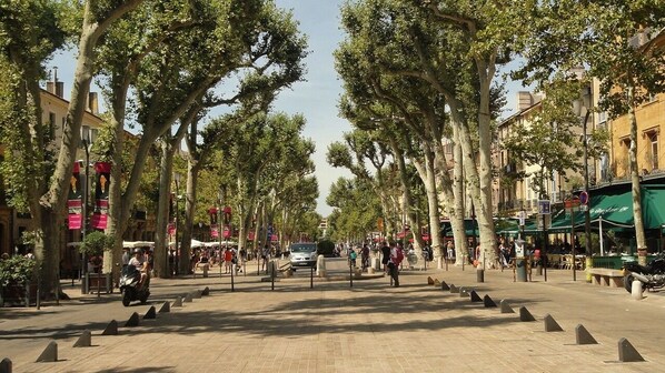 A tree-lined street with outdoor seating and a white van parked in the distance. - Renovated 2-room apartment with a balcony and private parking space (Aix-en-Provence)