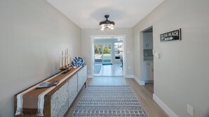 A hallway with a wooden console table, decorative items, a patterned rug, and a sign indicating a beach direction.