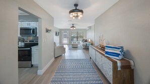 A modern kitchen with built-in appliances, a dining area with a wooden table and chairs, and a hallway leading to a living room with a sofa and a TV.
