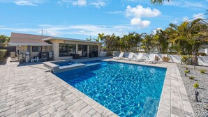 A swimming pool with lounge chairs, a covered patio, and palm trees.