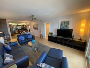 Una sala de estar moderna con un conjunto de sofás, una mesa de centro, un televisor de pantalla plana y un comedor al fondo.