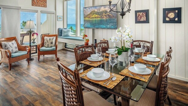 Un coin repas avec une table en verre dressée pour six personnes, entourée de chaises en osier.