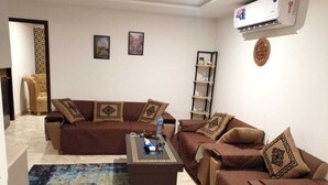 A living room with a sectional sofa, a coffee table, and a bookshelf. - Captivating 1-bed Apartment Fully Furnished (Lahore)