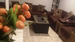 A living room with a sofa set, a coffee table, and a vase with orange flowers. - Captivating 1-bed Apartment Fully Furnished (Lahore)