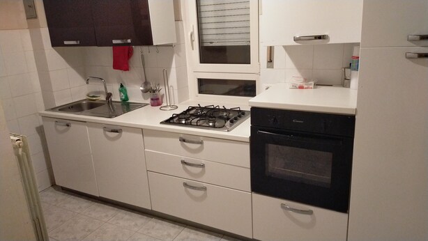 A compact kitchen with white cabinets, a gas stove, a built-in oven, a sink, and a window with blinds. - House of roae (Terni)