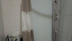 A small, enclosed shower area with a showerhead and a curtain. There is a shelf with toiletries next to the shower. - House of roae (Terni)
