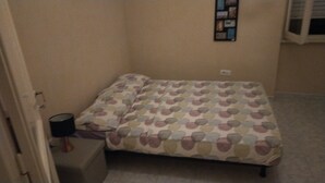 A small, dimly lit room with a bed covered in a polka dot blanket, a small table with a lamp, and a wall-mounted clock. - House of roae (Terni)