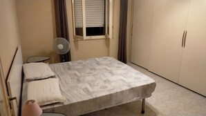 A small bedroom with a bed, a fan, a window with blinds, and a wardrobe. - House of roae (Terni)
