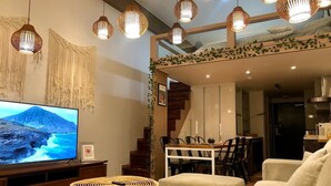 Ein modernes Wohnzimmer mit einem großen Flachbildfernseher, Rattanmöbeln und Pendelleuchten.