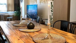 Ein Essbereich mit einem Holztisch, gewebten Tischsets, hängenden Pendelleuchten, einer Kerze und einem gerahmten Kunstwerk an der Wand.