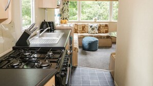 A compact kitchen with a gas stove, a sink, and a window providing natural light. - Vista (Moelfre)