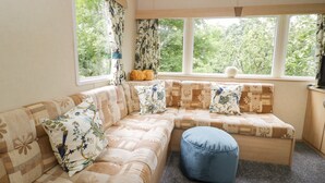 A cozy room with a sectional sofa, a blue ottoman, and large windows with curtains. - Vista (Moelfre)