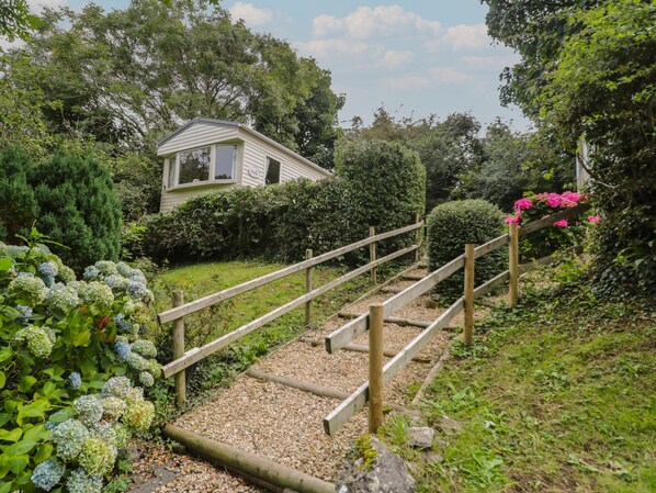 A wooden staircase leading to a house surrounded by lush greenery and flowering plants.