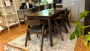 Eine moderne Küche mit einem Holzespeisetisch und Stühlen, einem weißen Regal und einem gemusterten Teppich.