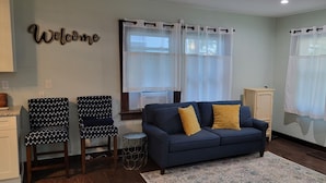 A living room with a dark blue sofa, two patterned chairs, a small round table, and a 'Welcome' sign on the wall. - KC Tiny Studio (Kansas City)