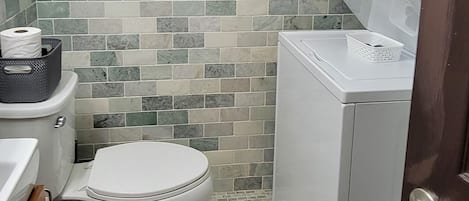 A compact bathroom with a toilet, a washing machine, and a tiled backsplash.