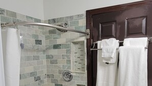 A bathroom with a shower, tiled walls, a door with towels, and a white washing machine. - KC Tiny Studio (Kansas City)