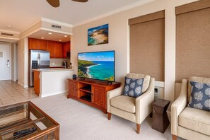 A living room with a TV, a sofa, a chair, a coffee table, and a kitchen area.