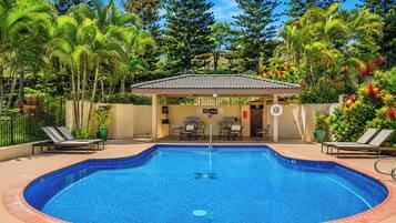 Piscina con sillas de descanso, zona de estar cubierta y exuberante vegetación tropical.