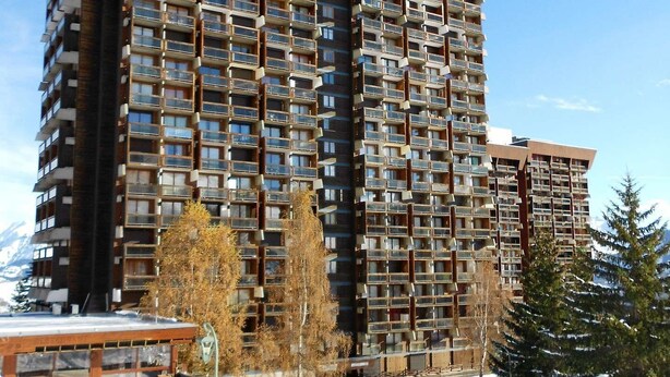 Un immeuble de grande hauteur doté de nombreux balcons, entouré de neige et d’arbres.