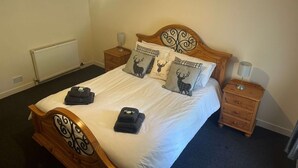 A neatly made bed with a wooden headboard, two bedside tables with lamps, and decorative pillows with deer designs. - 3 Bedroom Miners Cottage - Wanlockhead D & G (Wanlockhead)