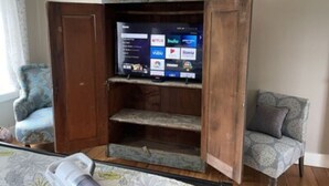 Un salon avec un meuble de rangement en bois pour les appareils multimédias, un téléviseur diffusant des services de streaming et deux fauteuils à motifs.