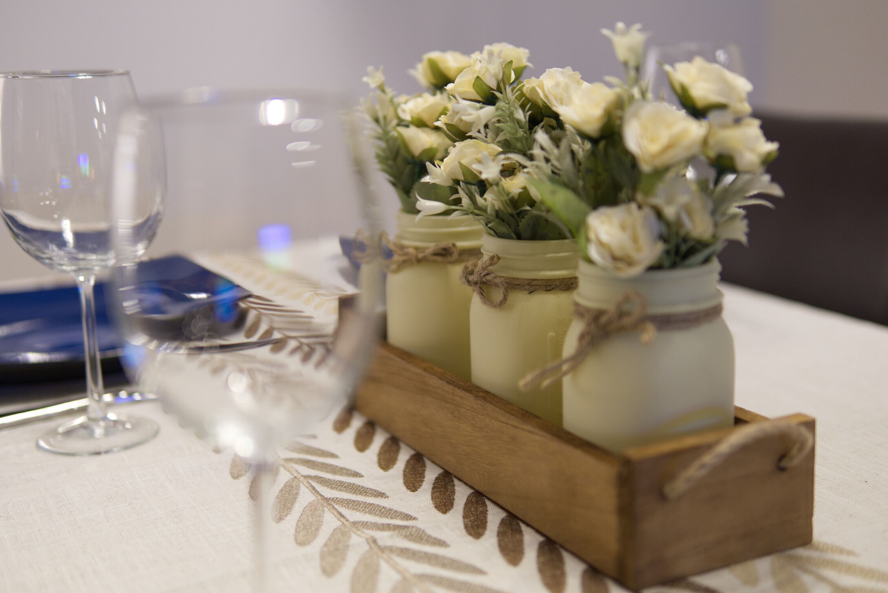 A table setting with a wine glass, a floral arrangement in mason jars, and a wooden tray.