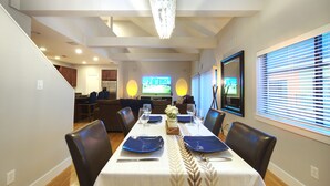 A dining area with a table set for four, chairs, a chandelier, and a television in the background. - Houston Heights Lux 3 story-townhouse-Rice Military (Houston)