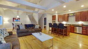 A spacious living area with a sofa, coffee table, and a kitchen with wooden cabinets and stainless steel appliances. - Houston Heights Lux 3 story-townhouse-Rice Military (Houston)