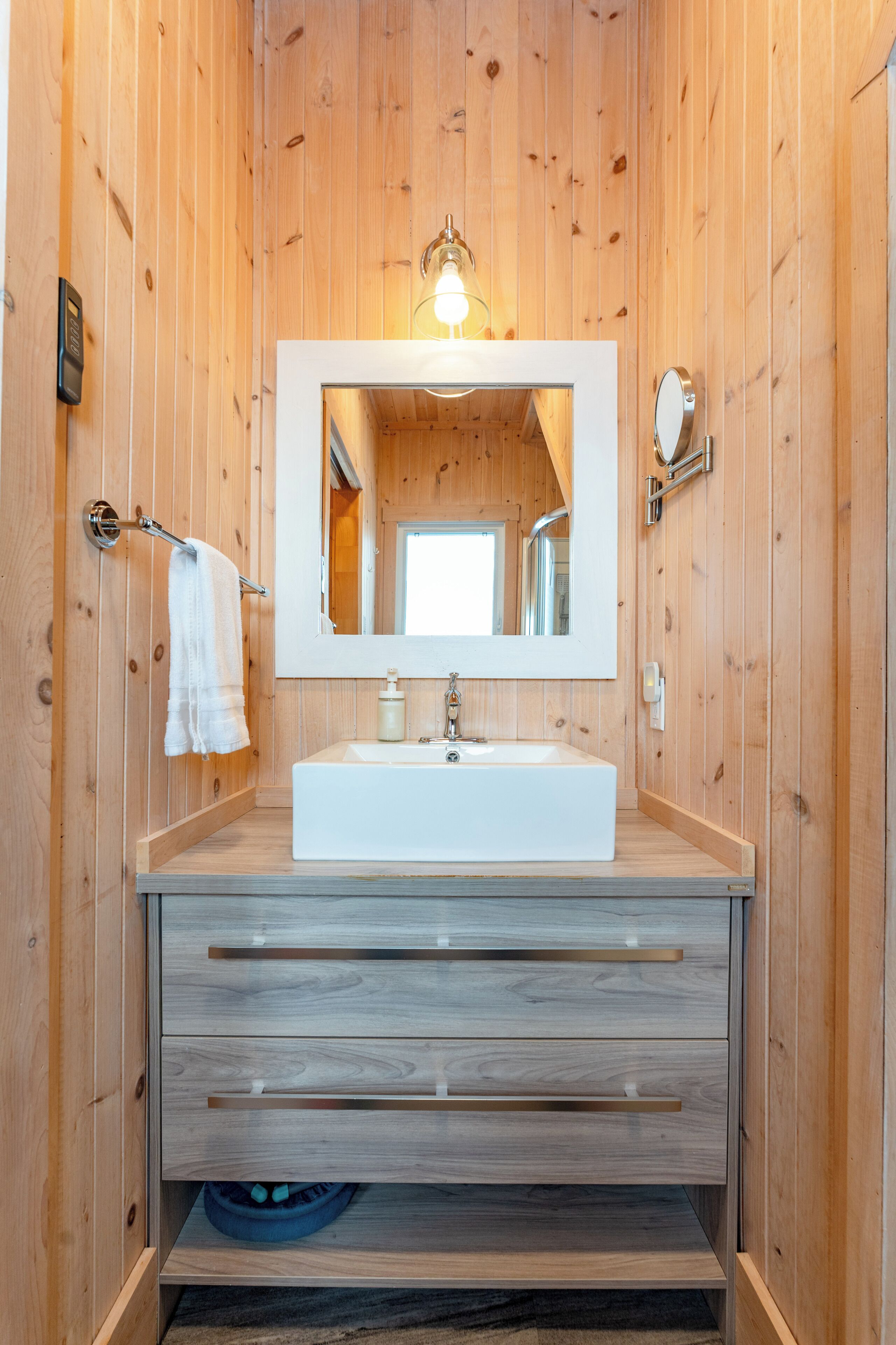 Ein Badezimmer mit Holzwänden, einem weißen Waschbecken, einem großen Spiegel und einem Handtuchhalter.