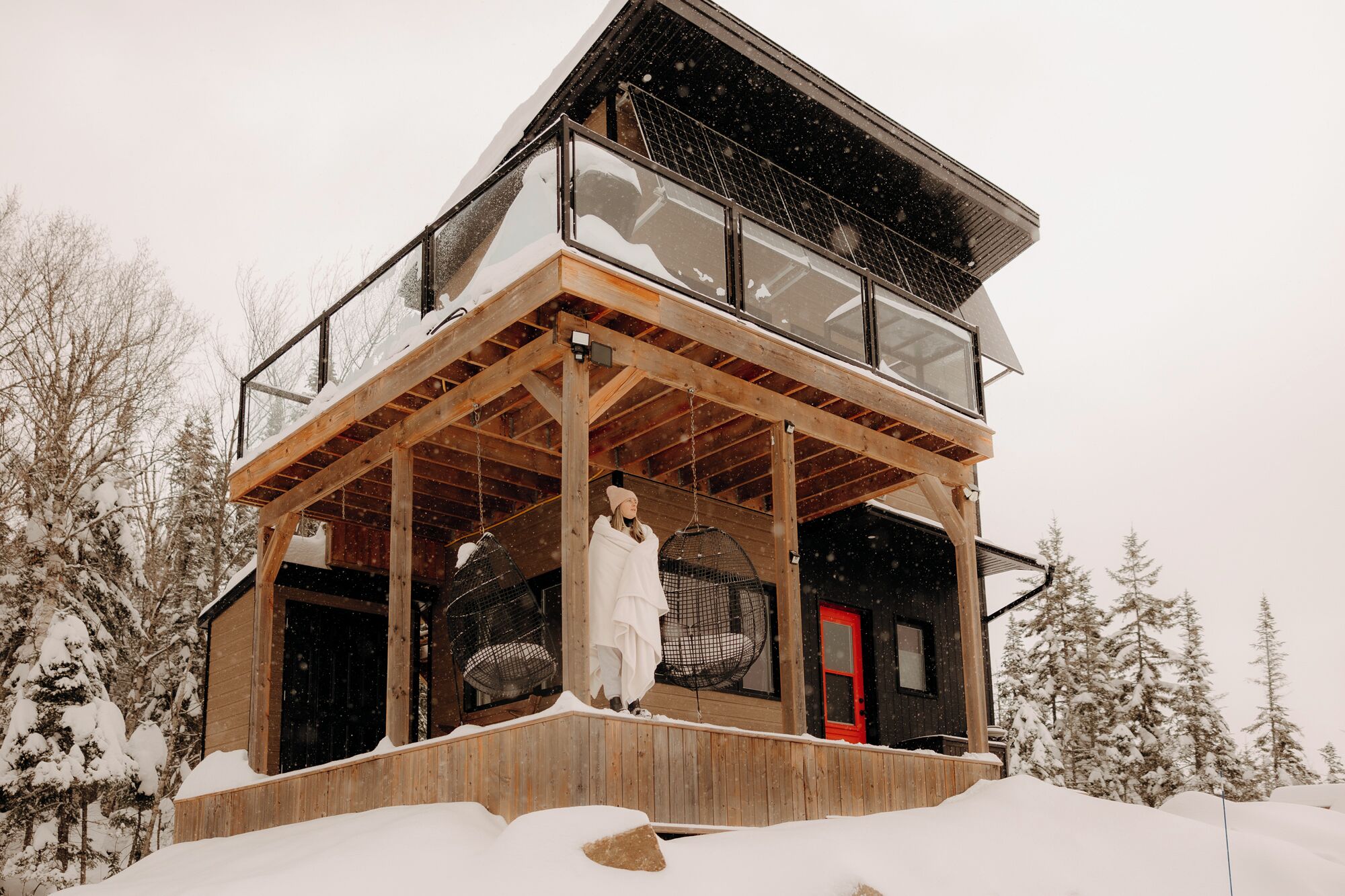 A two-story wooden cabin with a balcony and a red door.