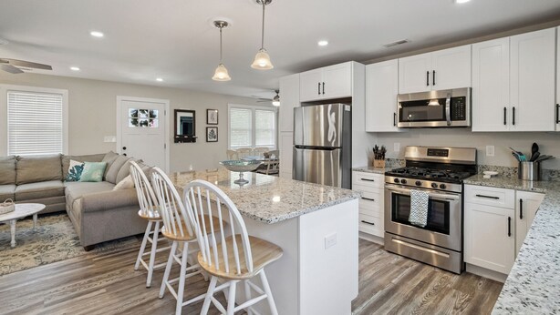 A modern kitchen with white cabinets, stainless steel appliances, and a central island with bar stools. - Private Saltwater Pool + Spacious Yard. King Suite and Linens & Towels Included! (Villas)