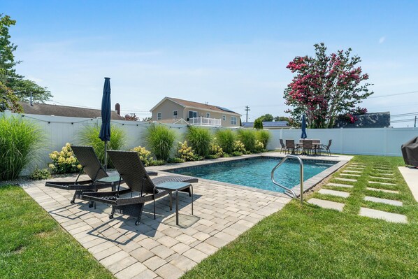 A backyard with a swimming pool, lounge chairs, and a patio table.