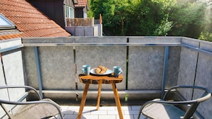 A balcony with a table set for two, a croissant, and two cups. - Modern, cozy & central - kitchen, parking space, Netflix & more (Pfaffenhofen an der Ilm)