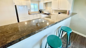 A modern kitchen with white cabinets, a granite countertop, and two teal bar stools. - NEW Two Bedroom Lake Getaway! Serene and CLEAN! (Hot Springs)