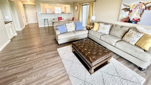 A living room with a sectional sofa, a tufted ottoman, and a dining area in the background. - NEW Two Bedroom Lake Getaway! Serene and CLEAN! (Hot Springs)