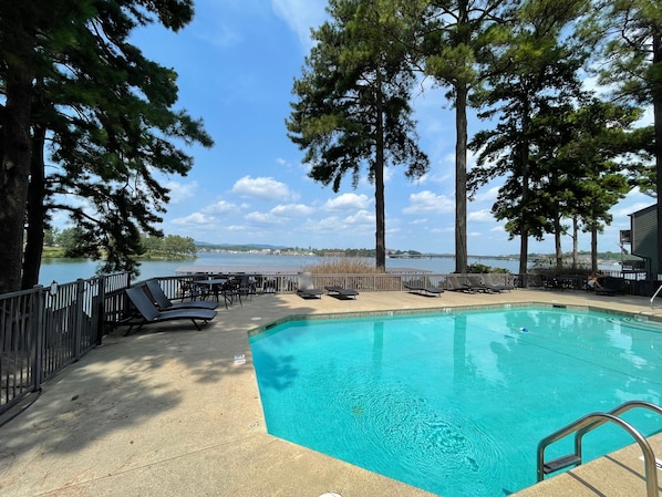 A pool area with lounge chairs and a view of a lake.