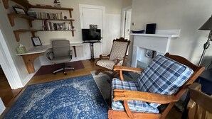 Uma sala de estar com uma cadeira de madeira, um sofá azul estampado, uma televisão e estantes de livros.