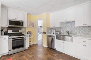 A modern kitchen with white cabinets, stainless steel appliances, and a wooden floor.